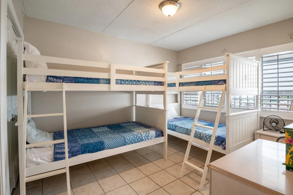 A playful and cozy bunk room with two sets of twin-over-twin bunk beds, cheerful textiles, and windows letting in lots of natural light. The room is designed for fun and togetherness, perfect for kids to enjoy late-night chats or morning play.