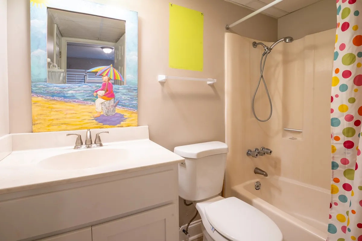 A light-hearted, beach-themed bathroom with a colorful shower curtain, vanity sink, and decorative mirror. The room feels fresh and inviting, suitable for both adults and children to enjoy convenient self-care routines.