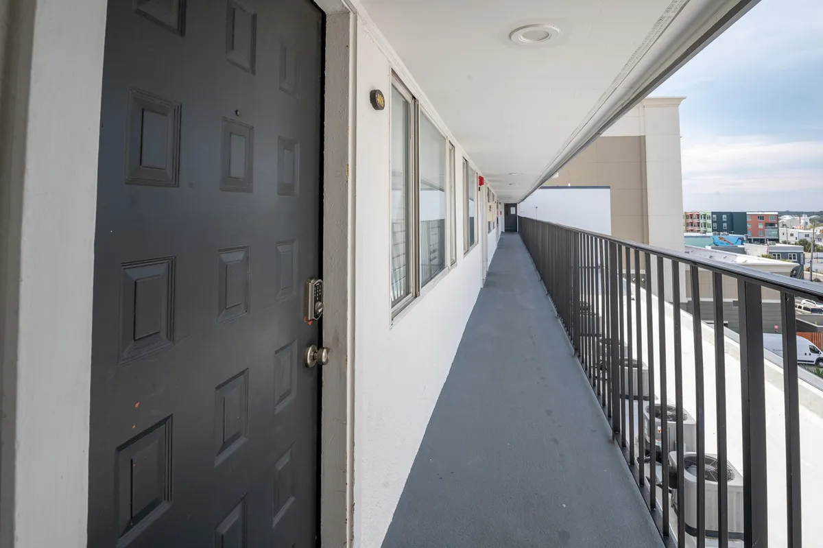 The shot highlights the welcoming entrance of the property with a distinctive black door, tidy railing, and sidewalk, suggesting an inviting arrival experience. The presence of other guests hints at a friendly, communal atmosphere within a secure, well-maintained environment.