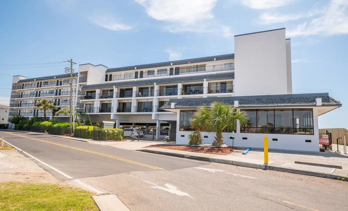 This image features the exterior of a modern condo building framed by swaying palm trees, with several balconies that capture the promise of sunset views and private relaxation. The inviting pool area hints at opportunities for leisure and socializing, while the tranquil street scene connects the property to the larger neighborhood vibe.