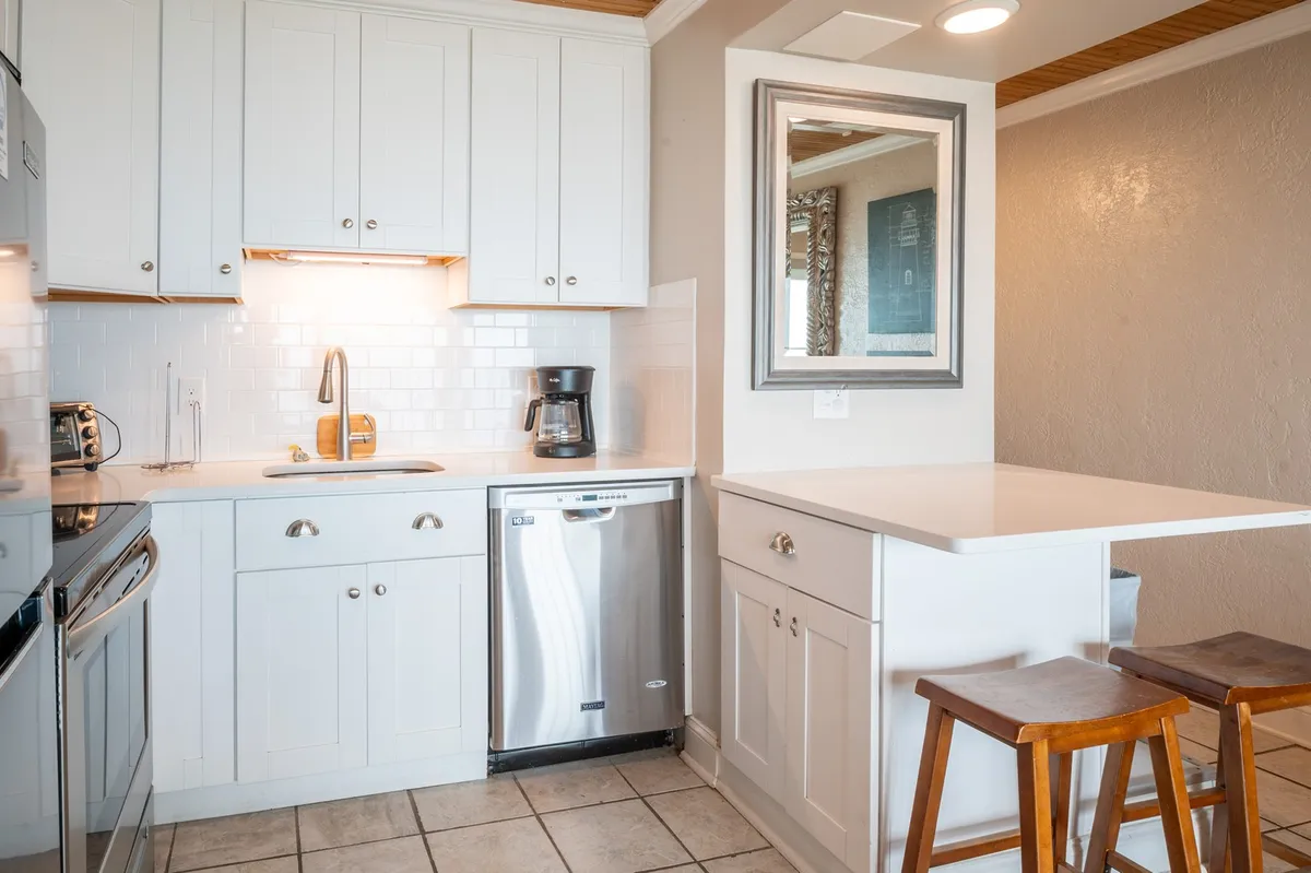 Featuring white cabinetry, stainless steel appliances, and a comfortable kitchen island, this kitchen scene suggests a cozy, communal space ideal for cooking, entertaining, or enjoying a morning coffee together.